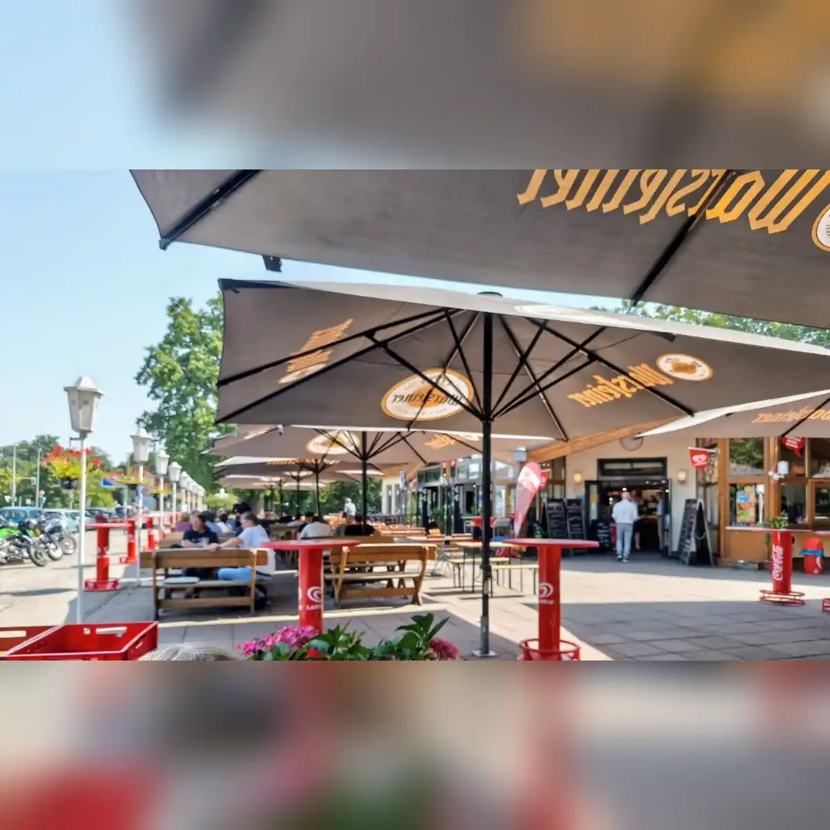 Sonniger Biergarten mit großen Sonnenschirmen, Holzbänken und Blumen