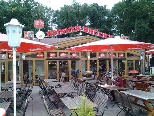 Terrasse der Spinner-Brücke mit roten Schirmen, Laternen und gedeckten Holztischen