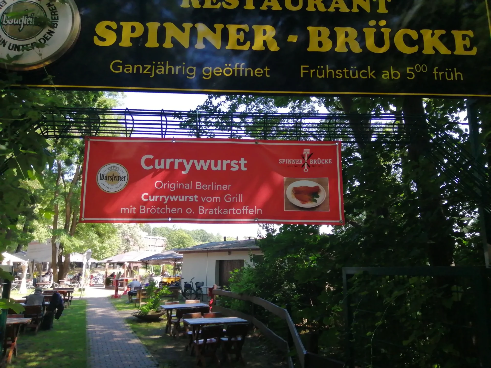Eingang des Restaurants Spinner-Brücke mit Schild und Currywurst-Banner im Sommer