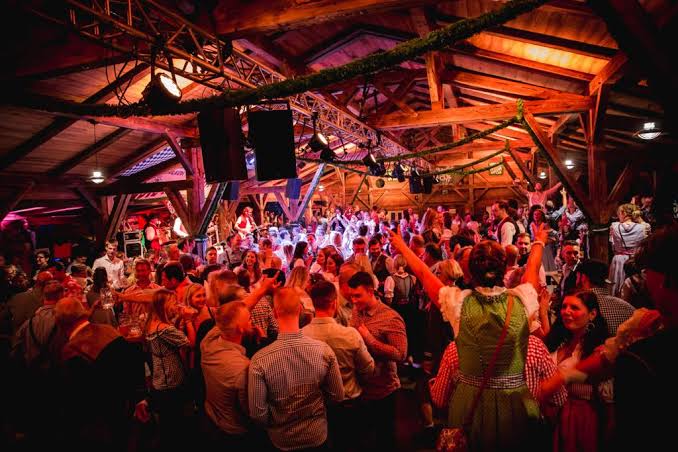 Gäste in Tracht feiern im festlich beleuchteten Stadl der Spinner-Brücke